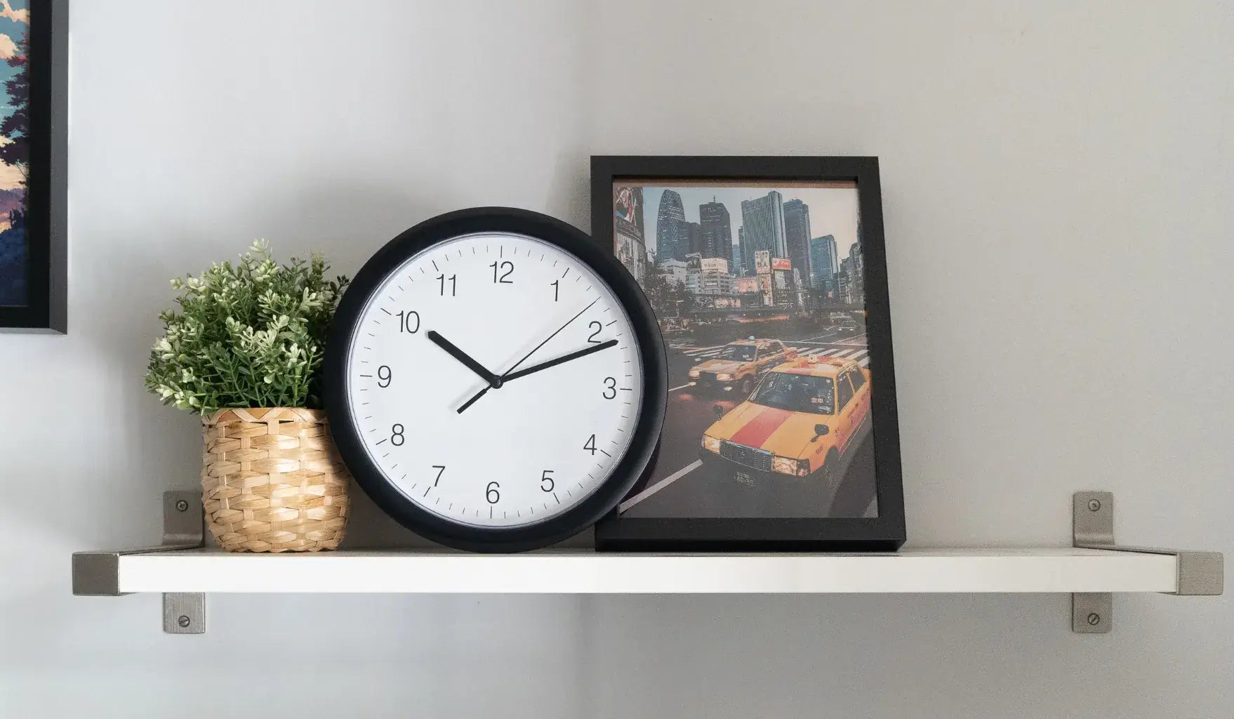 Black round wall clock on a white floating shelf styled with home decor