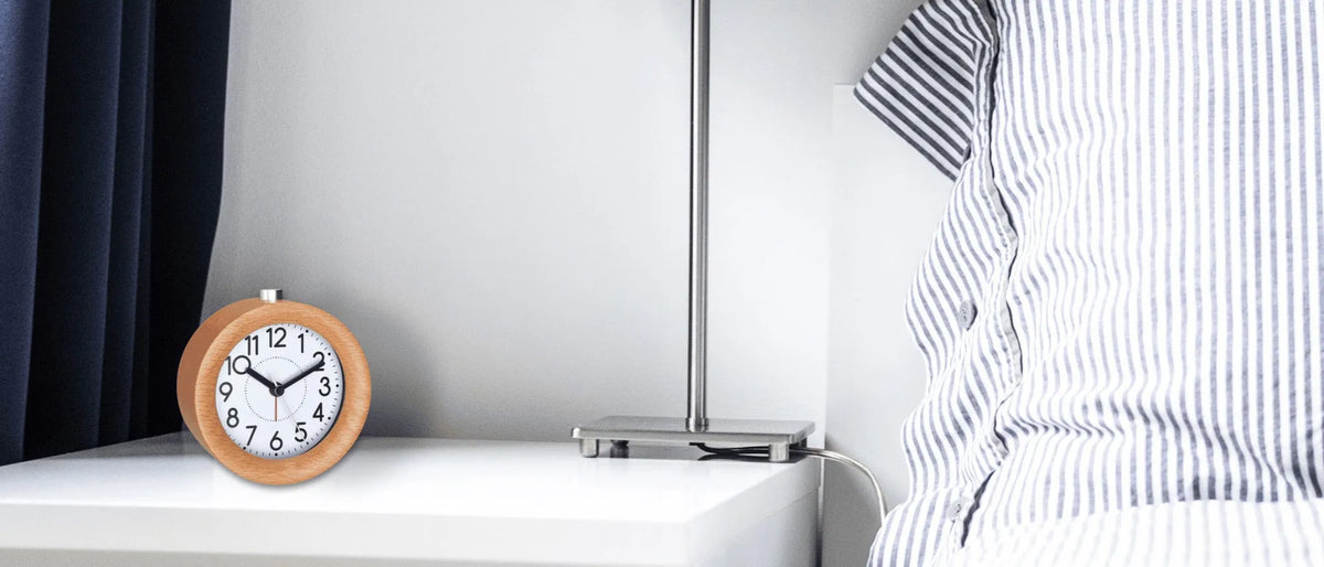 Wood-frame alarm clock on a white bedside table beside a lamp