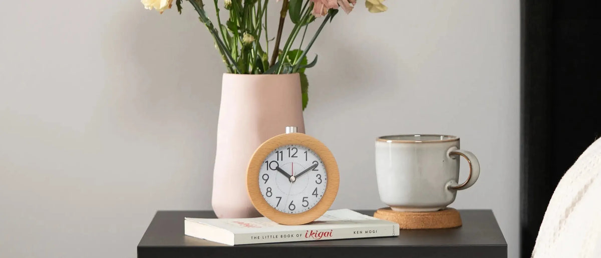 Wooden alarm clock on a bedside table with flowers and a cup of tea